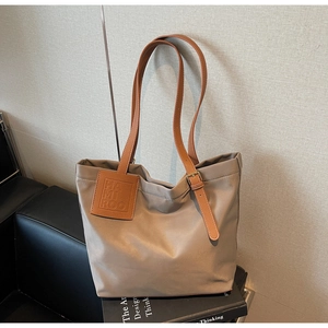 Close-up of khaki nylon tote bag with brown leather handles and engraved logo badge
