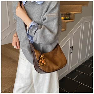 Close-up of brown suede hobo bag with wood bead charms and leather trim on a model