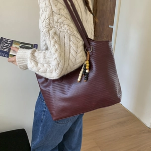 Detail of burgundy woven tote bag showing large capacity and colorful beaded charm