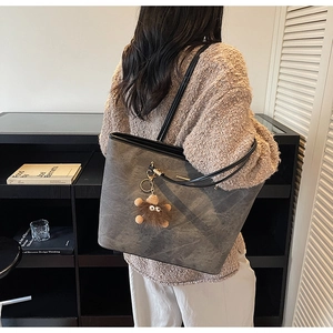 Detail of grey textured tote bag featuring black straps and a brown plush doll pendant