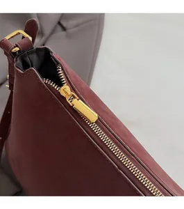 Close-up of smooth gold zipper and matte burgundy leather texture on a shoulder bag