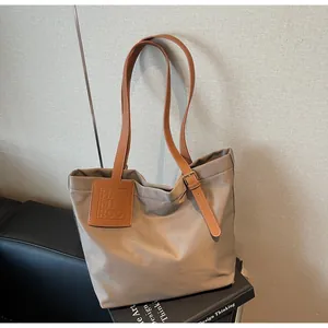 Close-up of khaki nylon tote bag featuring brown leather straps and branded square patch