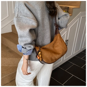 Detail of a brown suede half-moon underarm bag with unique beaded charm and knotted strap