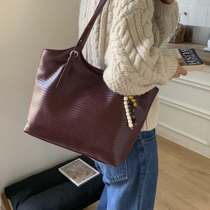 Detail of burgundy woven tote bag with wooden bead charm and adjustable strap