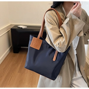 Detail of navy nylon tote bag with brown leather shoulder straps and logo patch