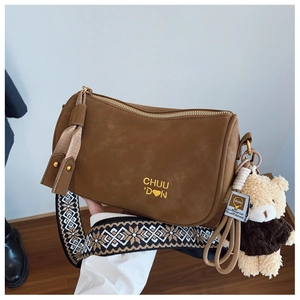 Détail du sac cylindre marron avec bandoulière tissée géométrique et breloque ours