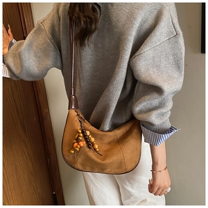 Detail of brown suede crescent bag with textured stitching and wooden bead tassel ornament