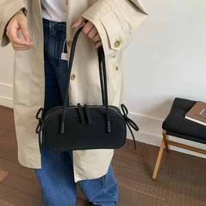 Détail du sac cabas noir avec nœud coulissant sur un mannequin en trench beige