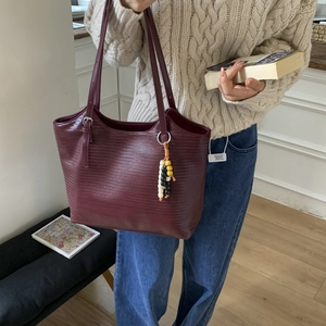 Detail of burgundy woven tote bag featuring colorful beaded tassel charm and shoulder strap