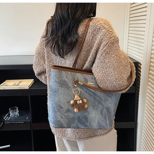 Detailed view of washed blue tote bag with brown leather handles and plush charm