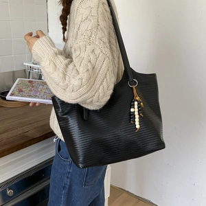 Detail of black woven tote bag featuring a decorative wood bead tassel on the shoulder strap