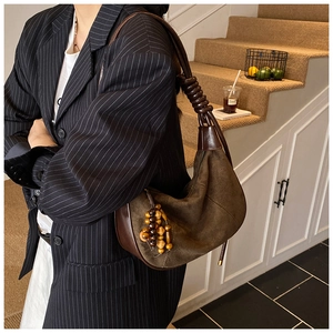 Close-up of brown suede underarm bag featuring twisted shoulder strap and beaded charm