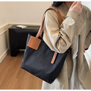 Detail of a large black tote bag with brown leather handles and brand logo patch