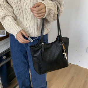 Close-up of black woven tote bag featuring silver buckles and stylish beaded tassel detail