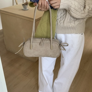 Détail du sac baguette beige mat avec nœuds décoratifs et longues anses d'épaule