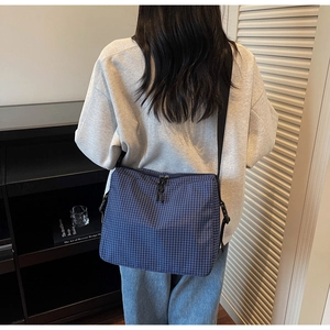 Close-up of blue plaid canvas tote bag with adjustable black strap and dual zippers