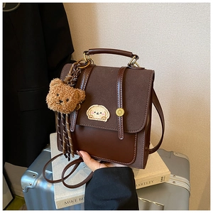Detail der braunen Ledertasche mit Hundestickerei und Plüschbär-Anhänger im Vintage-Stil