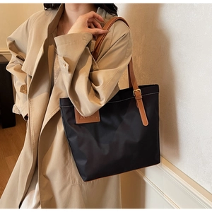 Detail of a black nylon tote bag with brown leather straps worn with a beige trench coat