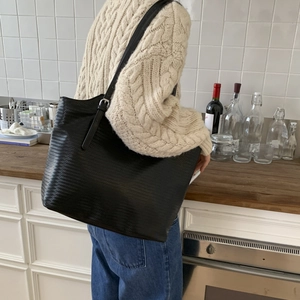 Detail of black textured tote bag featuring adjustable shoulder strap and silver hardware