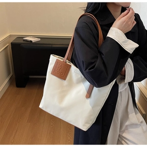 Detail of white tote bag with brown leather brand tag and reinforced handle stitching