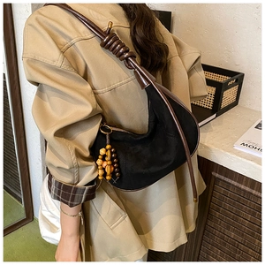 Detail of a black hobo bag with a brown knotted leather strap and wooden bead charm