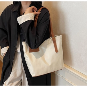 Detail of white tote bag featuring brown leather straps and gold metal buckle