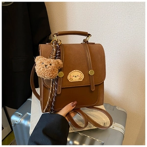 Brauner Retro-Rucksack mit Bärenanhänger auf Silberkoffer, lässig für den Alltag