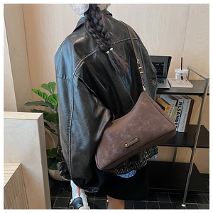 Detail view of the brown frosted leather crossbody bag with a gold metal logo plate