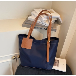 Detail of navy blue nylon tote bag with brown leather straps and branded label patch