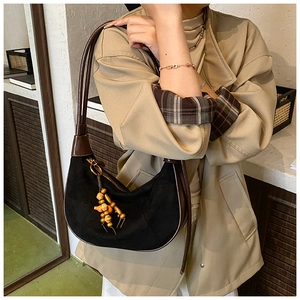 Detail of a crescent hobo bag in black suede with brown leather trim and wooden bead charm
