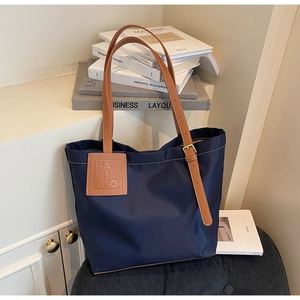 Detail of navy nylon tote bag showing leather handles, logo patch, and white contrast stitching