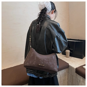 Detail of dark brown matte half-moon bag with golden metal logo plaque and fine strap
