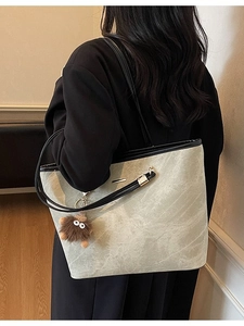 Large gray-green leather tote bag with black straps and a brown plush monster charm charm