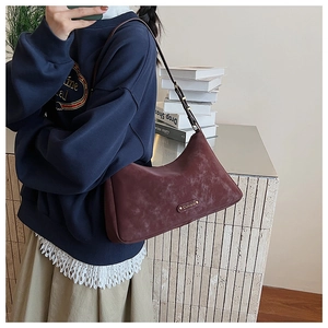 Detail of vintage matte burgundy shoulder bag featuring a sleek gold metal logo plate