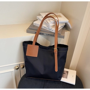 Close-up of navy nylon tote bag with brown leather straps and branded logo patch