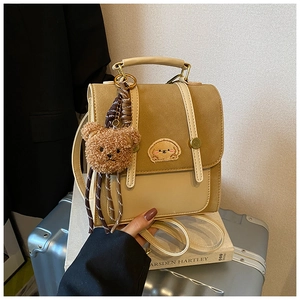 Detail eines zweifarbigen braunen Rucksacks mit Plüschbärenanhänger und Hundestickerei