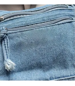 Detail of blue denim shoulder bag with white embroidery and fringed metal zippers