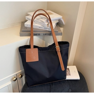 Detail of black nylon tote bag with brown leather straps and contrast white stitching