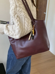 Deep burgundy tote bag with woven texture worn by model in a cozy indoor setting