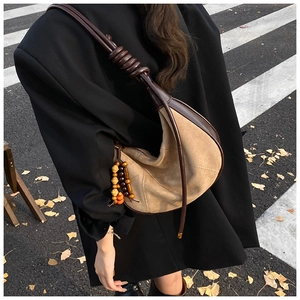 Close-up of beige suede crescent bag with rope knot strap and wood bead detail