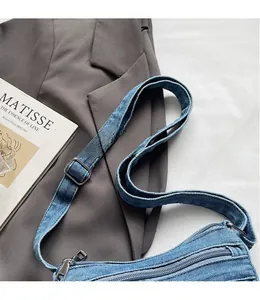Detail view of light blue washed denim shoulder bag with adjustable strap and metal zipper