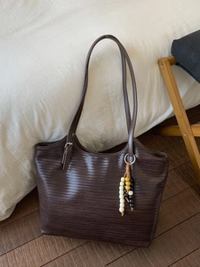 Retro dark brown woven tote bag with beaded tassel and adjustable strap on wood floor