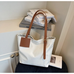 Detail of white nylon tote bag featuring brown leather straps and branded leather patch