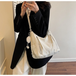 Detailed view of white large capacity tote bag with silver zippers and plush ball charm