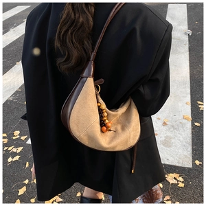 Beige suede crescent shoulder bag with brown leather trim and wooden bead charm accessory