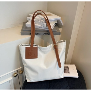 Close-up of minimalist white tote bag with adjustable brown leather straps and metallic buckle