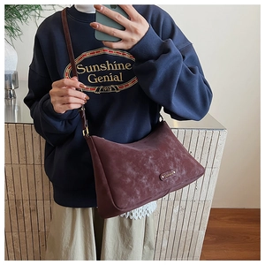 Close-up of vintage reddish brown frosted crossbody bag with metal logo detail on model