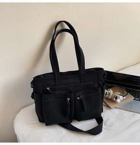 Close-up of black corduroy tote bag featuring two front zipper pockets and shoulder strap