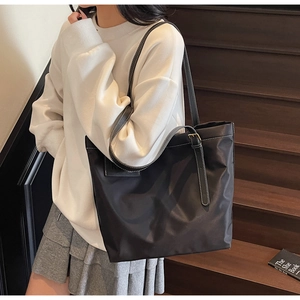 Detail of black nylon tote bag with leather strap and white contrast stitching