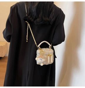 Detail of beige tweed bag with gold chain strap and cute plush charm on black blazer